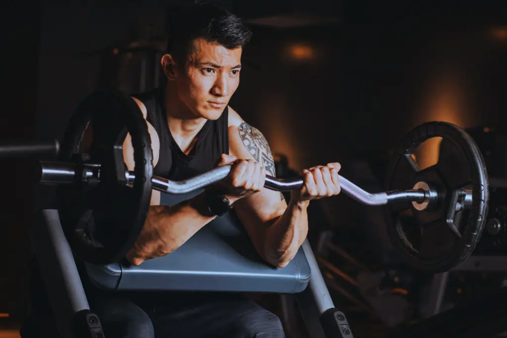 A man performing ez bar preacher curl in a gym.